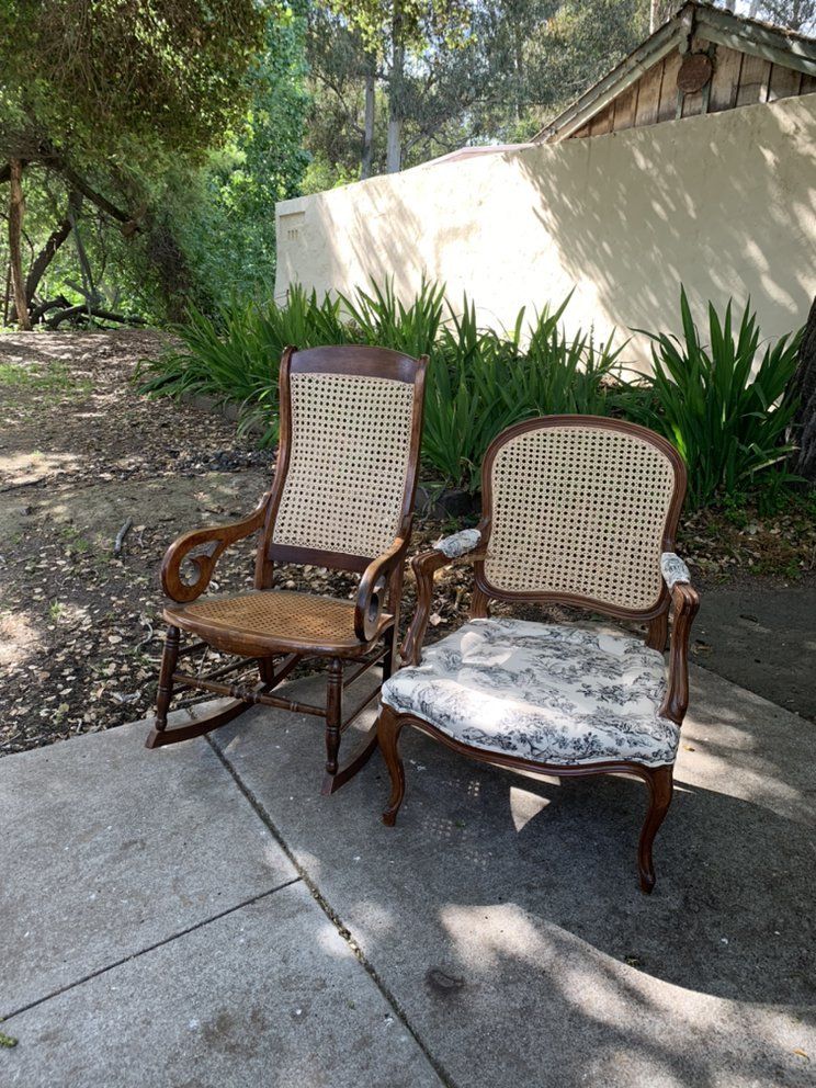 Two rocking chairs are sitting on a sidewalk in front of a house.