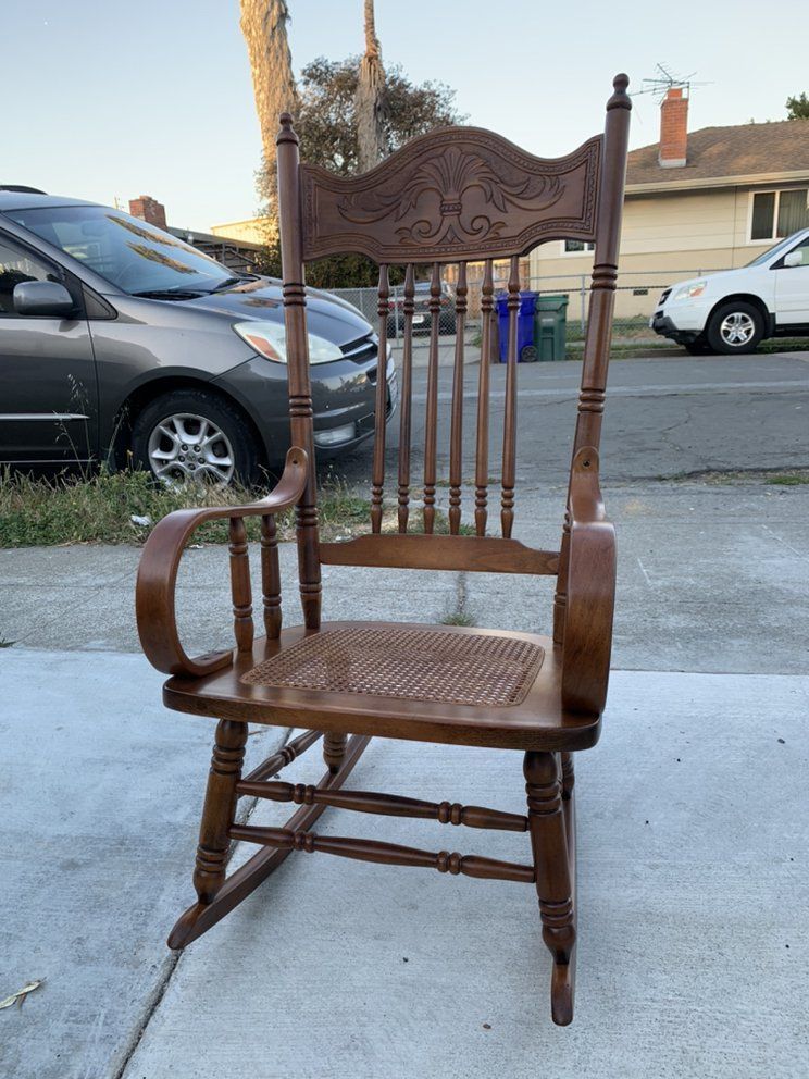 A wooden rocking chair is sitting on the sidewalk next to a car.