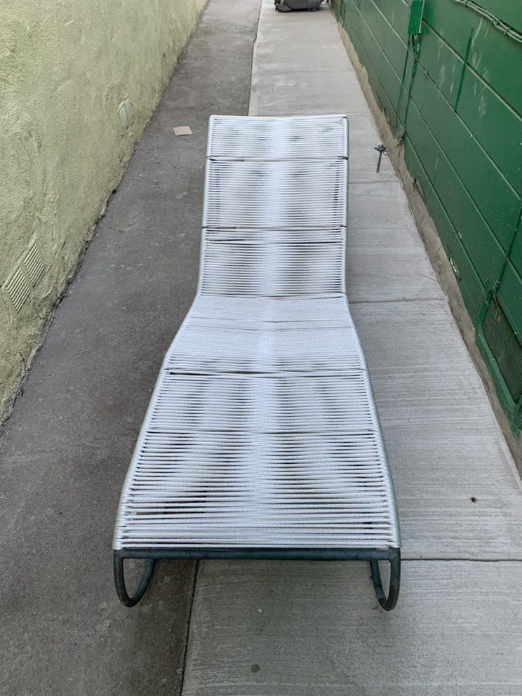 A white lounge chair is sitting on a sidewalk next to a green wall.