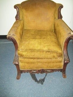 A chair with a broken arm rest is sitting on a carpet.