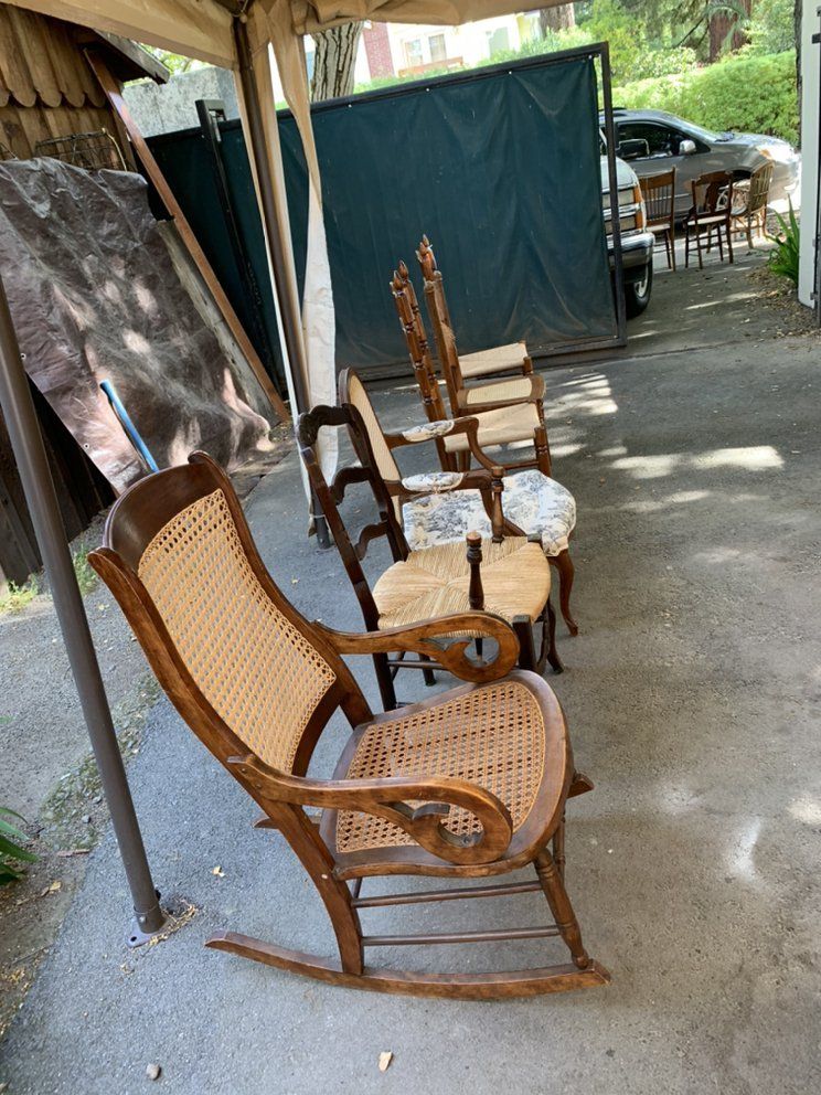 A row of wooden rocking chairs with wicker seats are sitting under a tent.