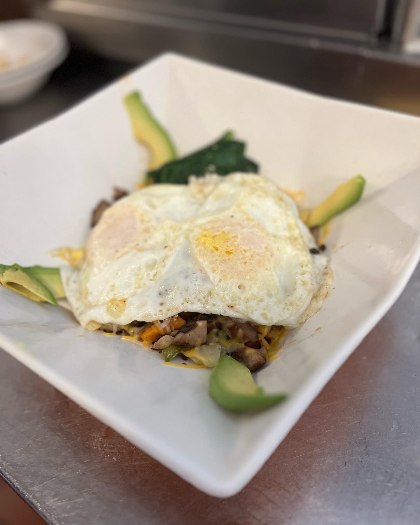 A white plate topped with eggs , avocado , spinach and mushrooms.