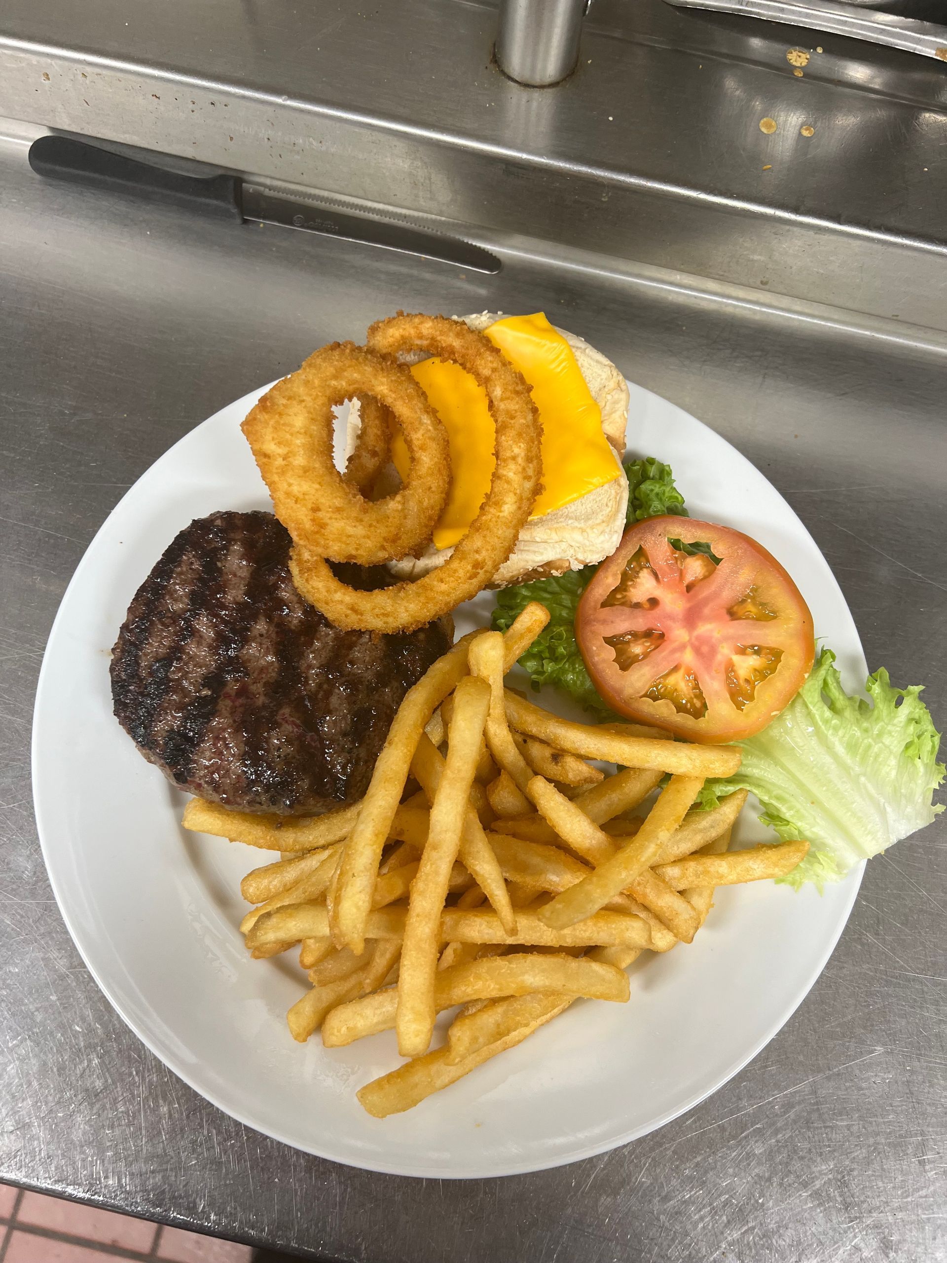 A white plate topped with a hamburger , onion rings , french fries and lettuce.