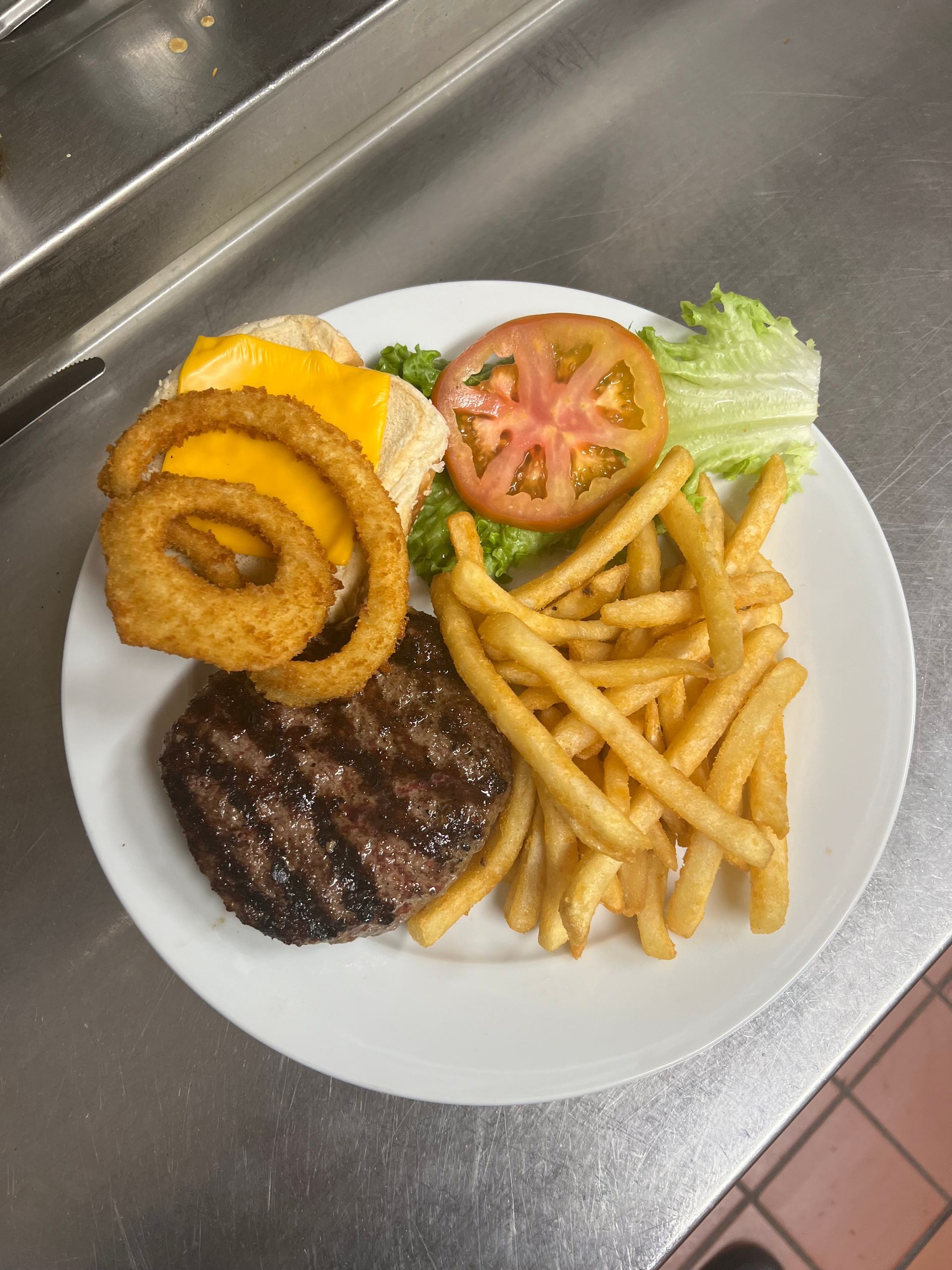 A white plate topped with a hamburger , onion rings , french fries and lettuce.