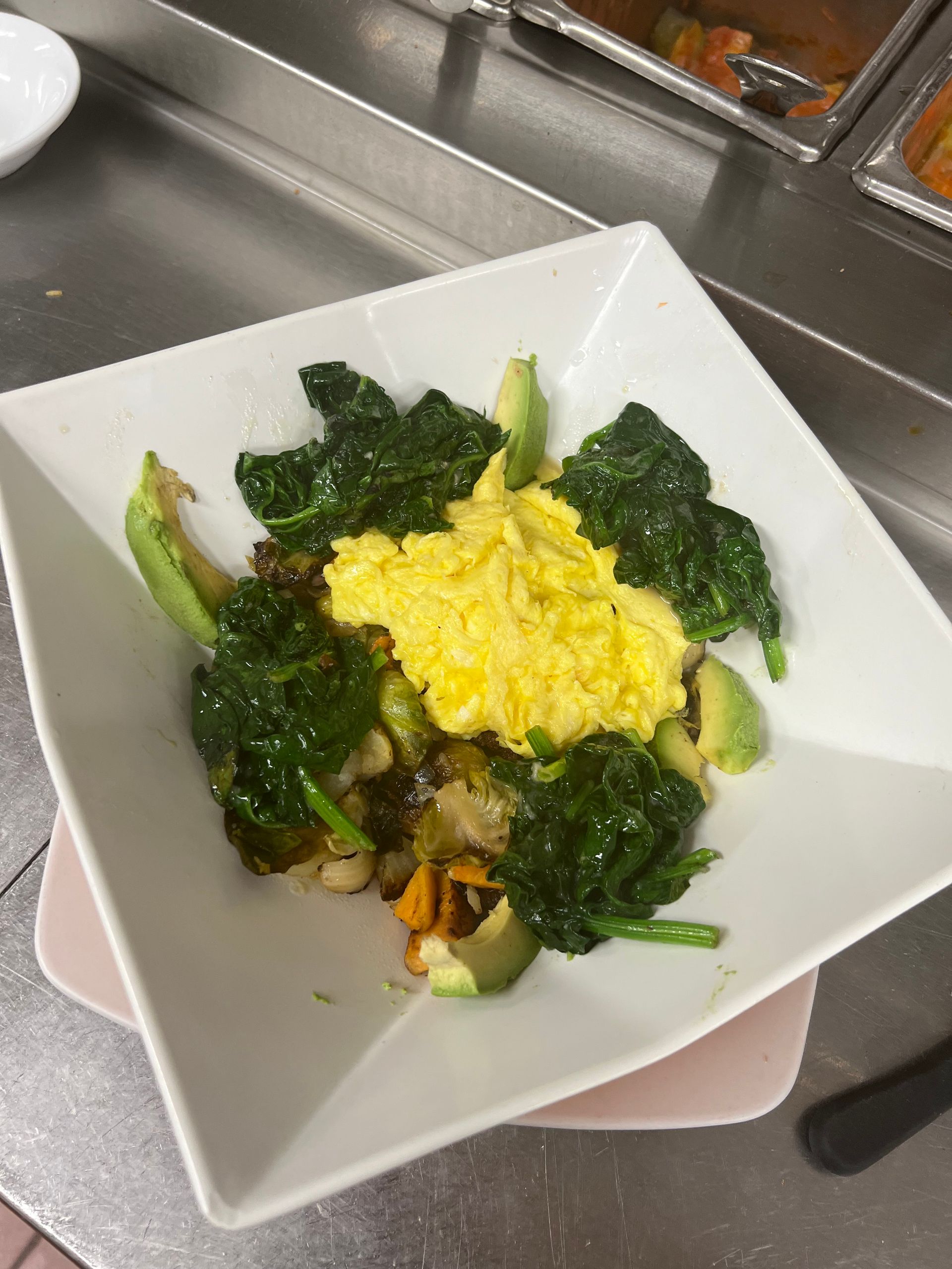 A white plate topped with scrambled eggs avocado and spinach