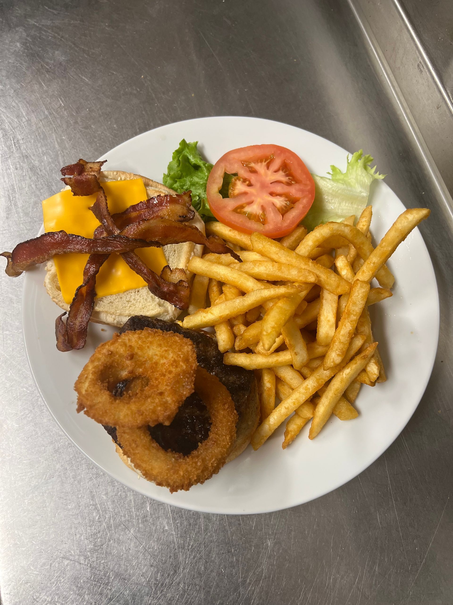 A white plate topped with a hamburger , french fries , onion rings and bacon.