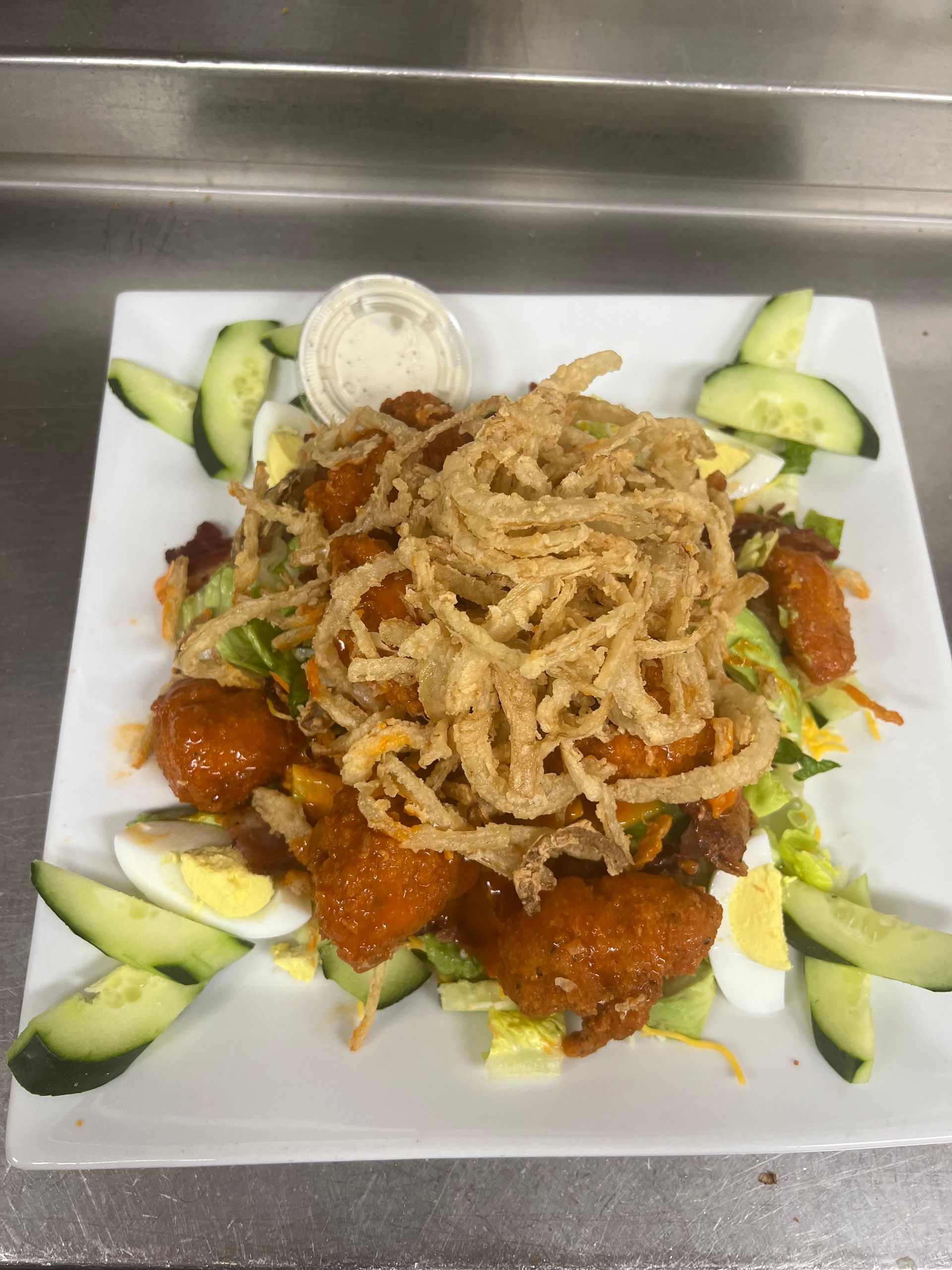 A salad with fried onions , cucumbers , eggs and chicken on a white plate.