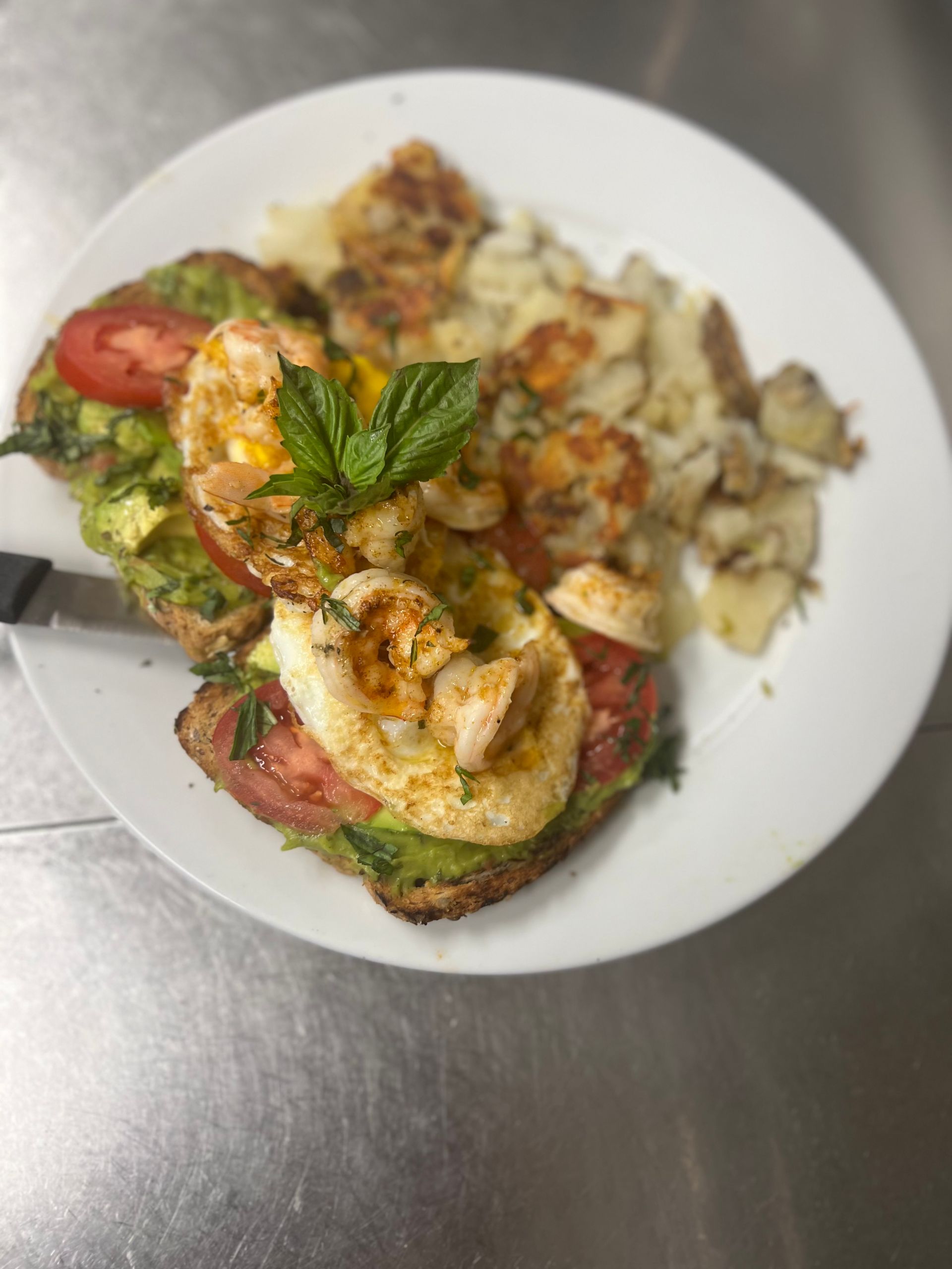 A white plate topped with a sandwich , shrimp , tomatoes and potatoes.