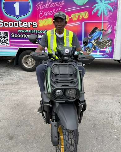 Man on scooter in front of a truck, wearing a safety vest.