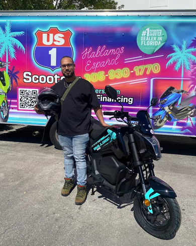 Man holding helmet next to a black scooter in front of a US 1 Scooters truck.