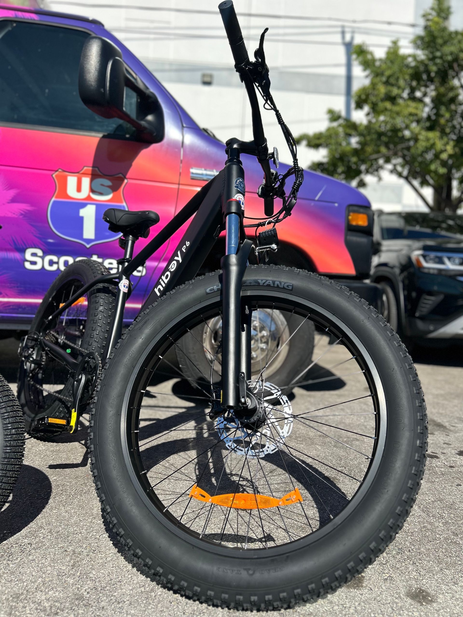Black electric fat tire bicycle parked in front of a colorful van, outdoors.