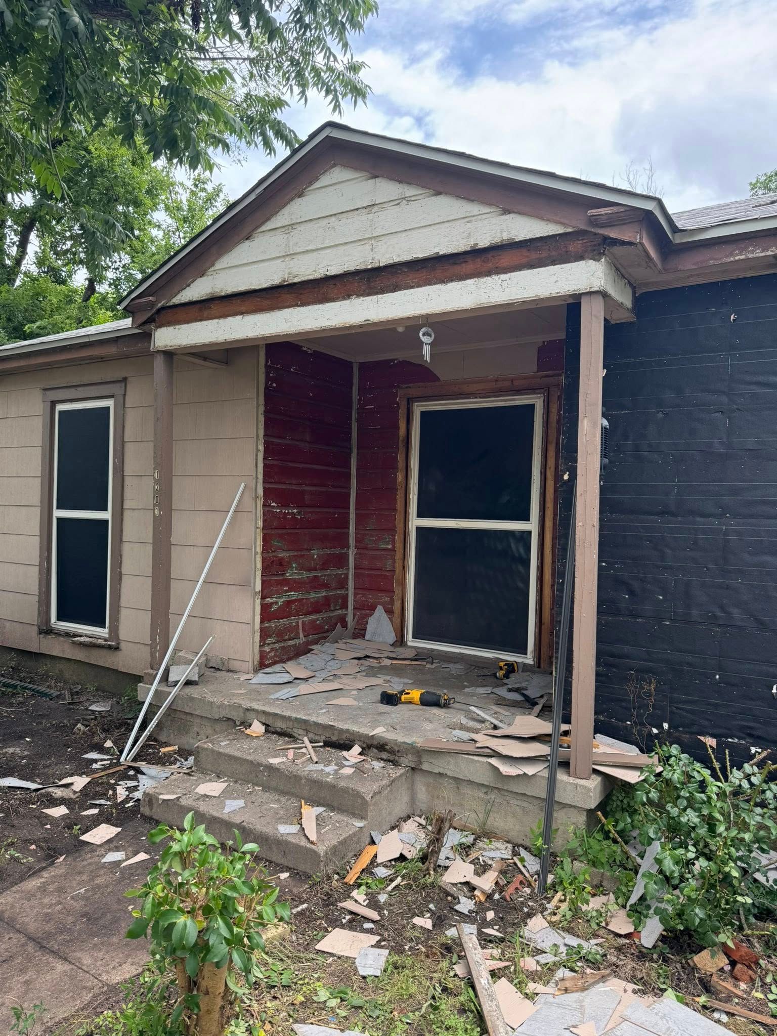 Exterior of a house undergoing renovation.  Concrete steps lead to the front door, with materials strewn about.