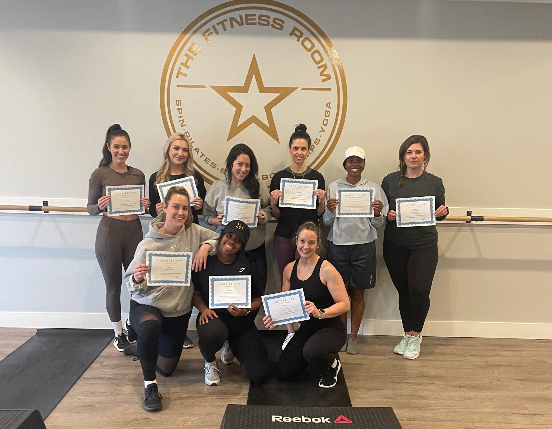 A group of women are posing for a picture in a gym holding certificates.