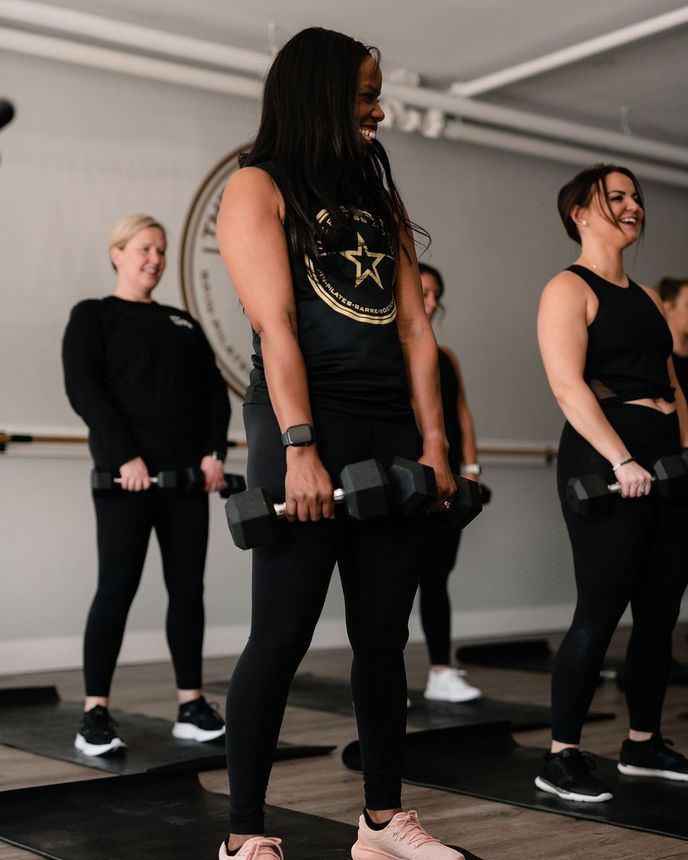 A group of women are standing on yoga mats holding dumbbells in a gym.