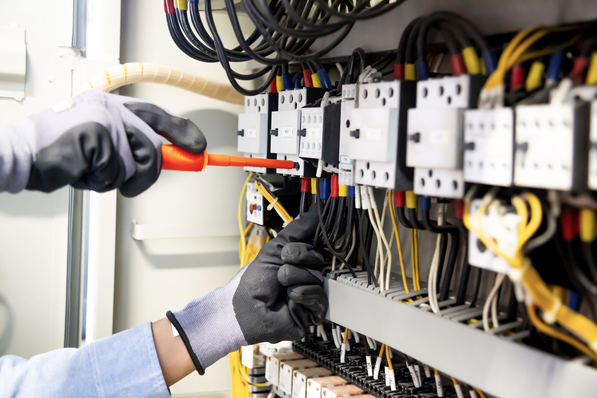An electrician is working on an electrical panel with a screwdriver.