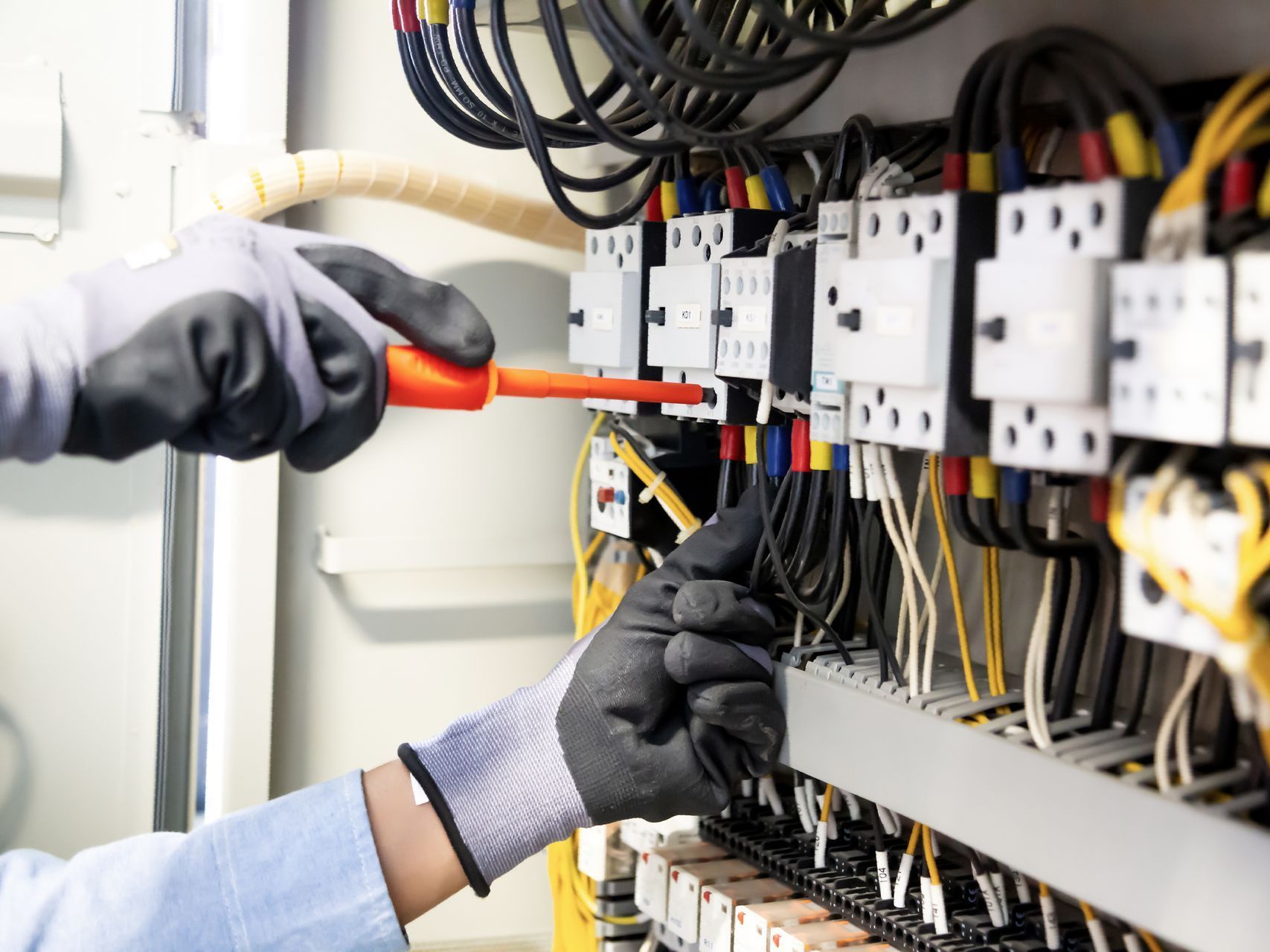 An electrician is working on an electrical panel with a screwdriver.