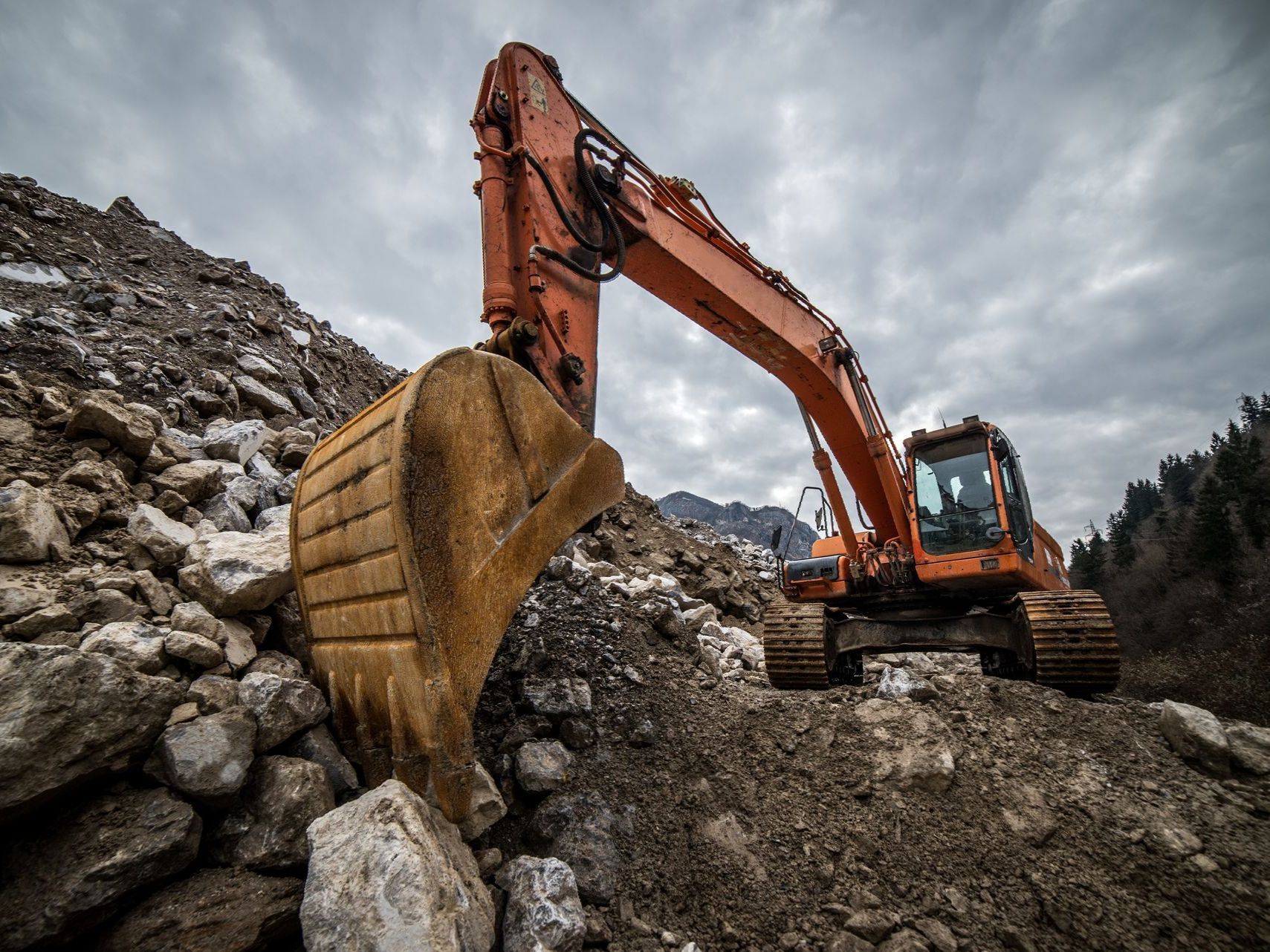 A large excavator is working on a rocky hillside.