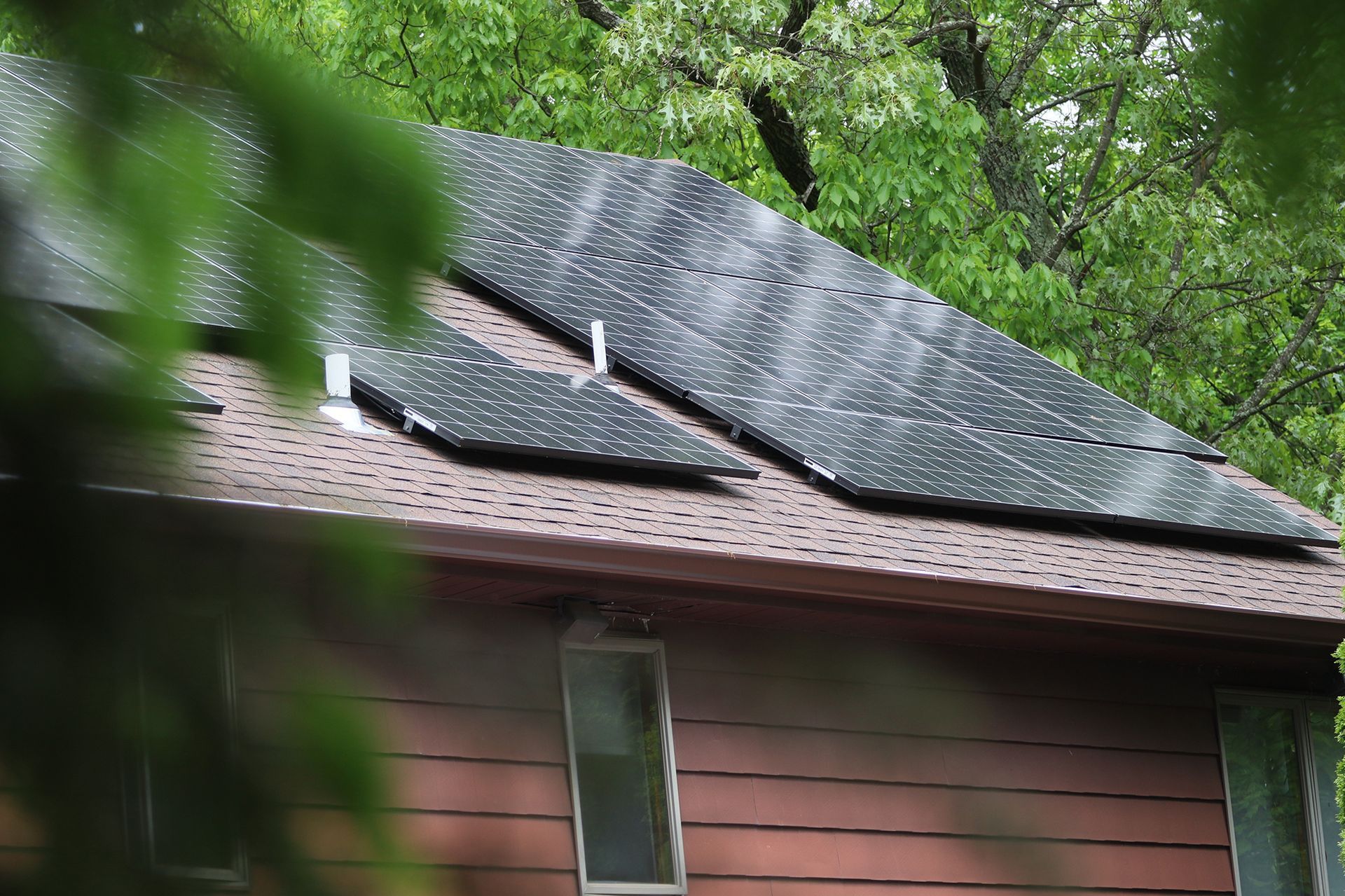 A house with solar panels on the roof is surrounded by trees.