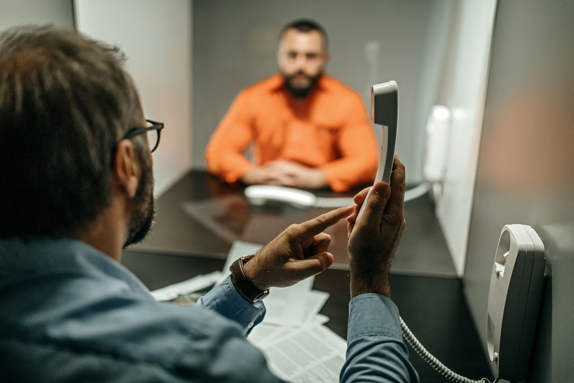 A man is talking on a telephone in front of a man in an orange shirt.