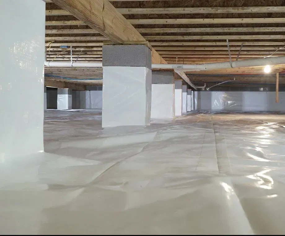 White crawlspace with plastic sheeting on the floor and pillars supporting the structure.