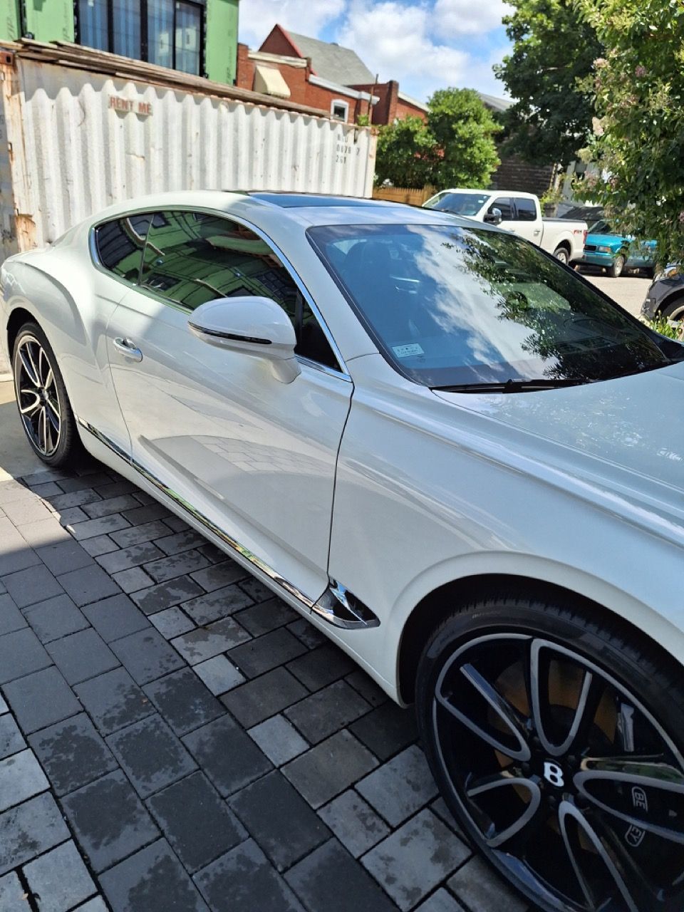 A white bentley continental gt is parked on a brick driveway.