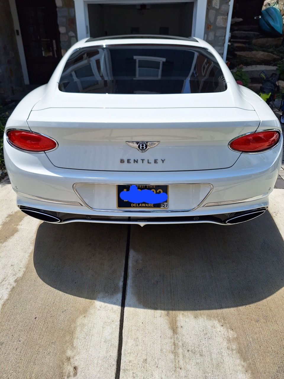 A white bentley is parked in a driveway in front of a house.