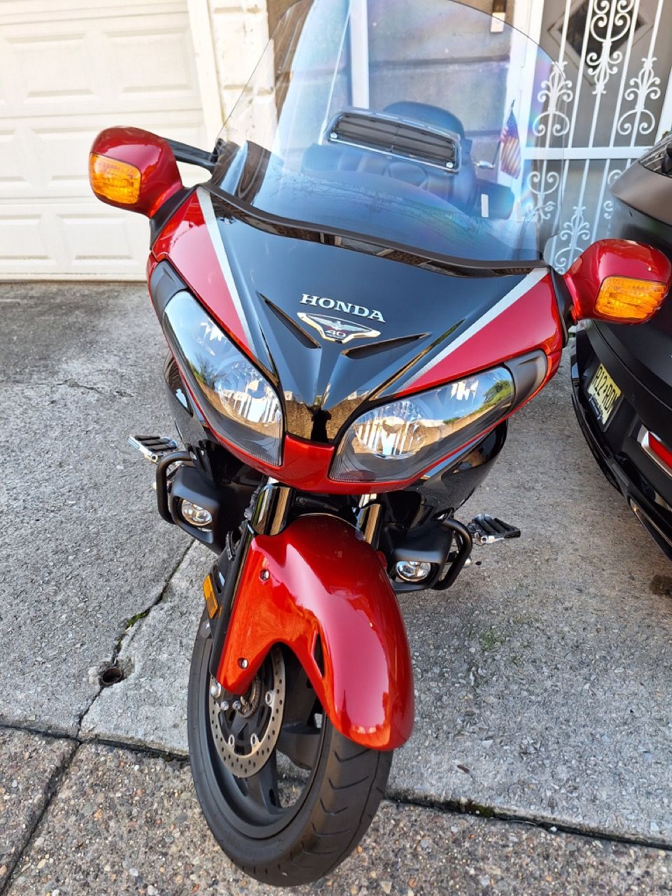 A red motorcycle with a windshield is parked in front of a garage door.