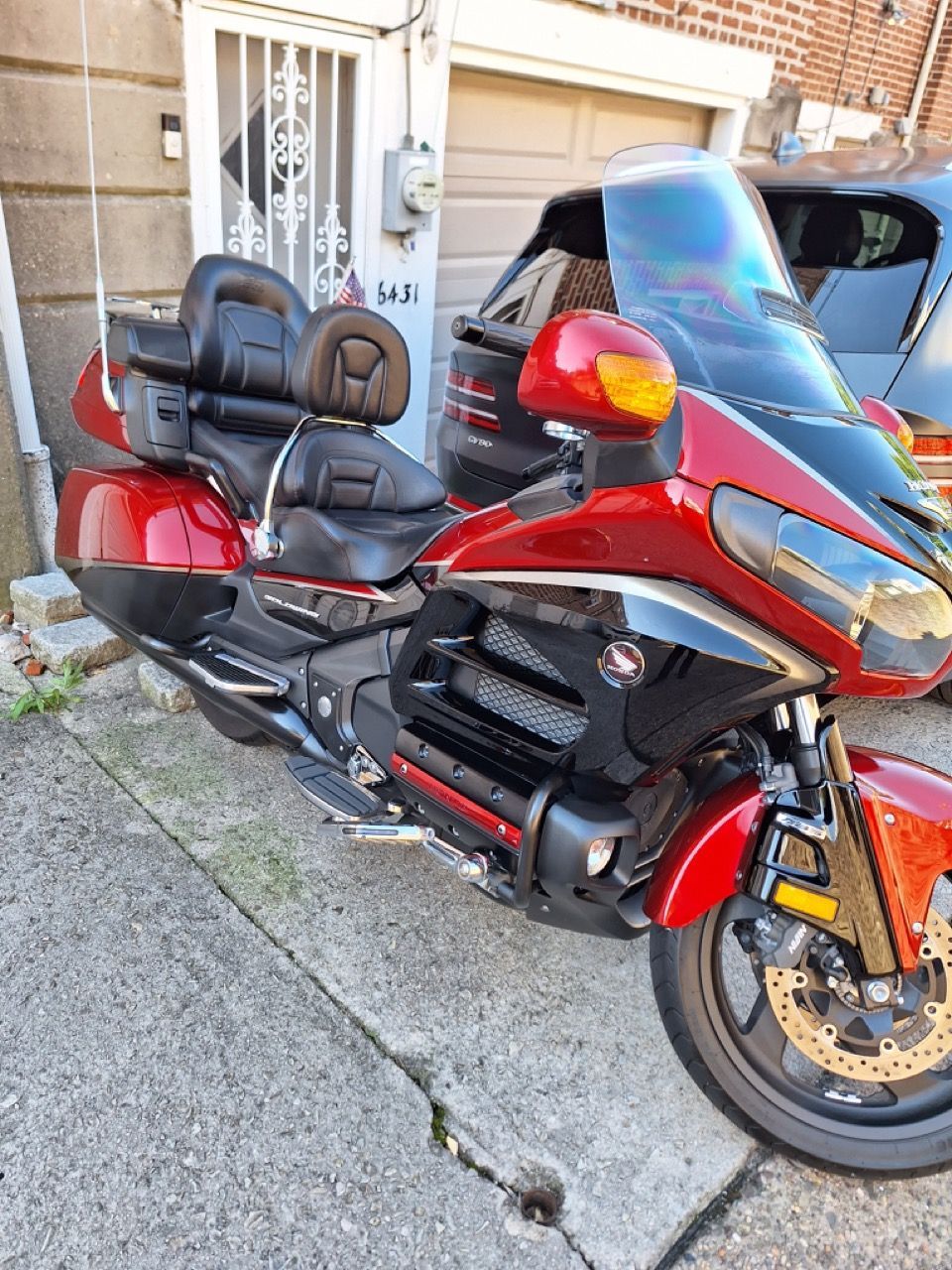 A red motorcycle is parked on the sidewalk in front of a garage.