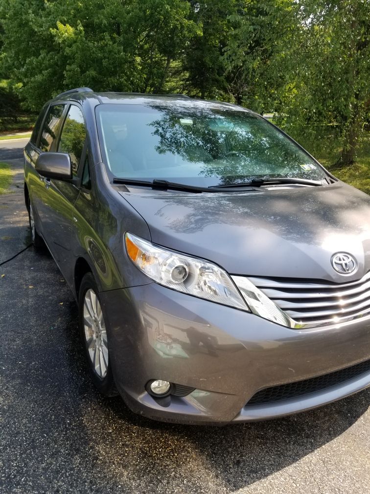 A gray toyota sienna minivan is parked on the side of the road.