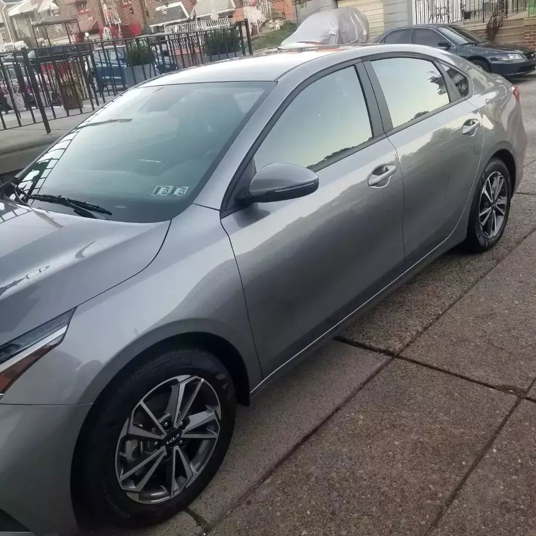 A silver car is parked on a sidewalk next to a fence.