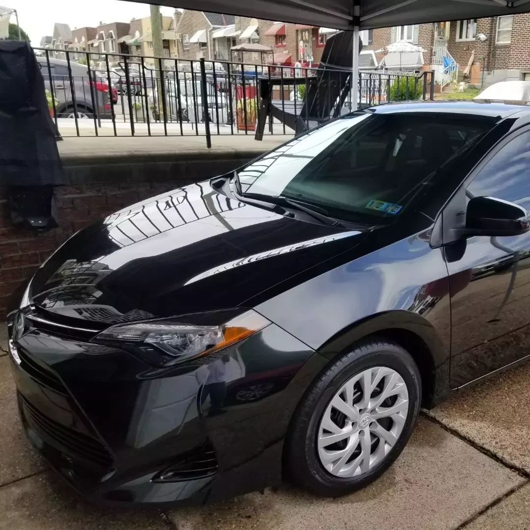 A black car is parked under a tent on a sidewalk.