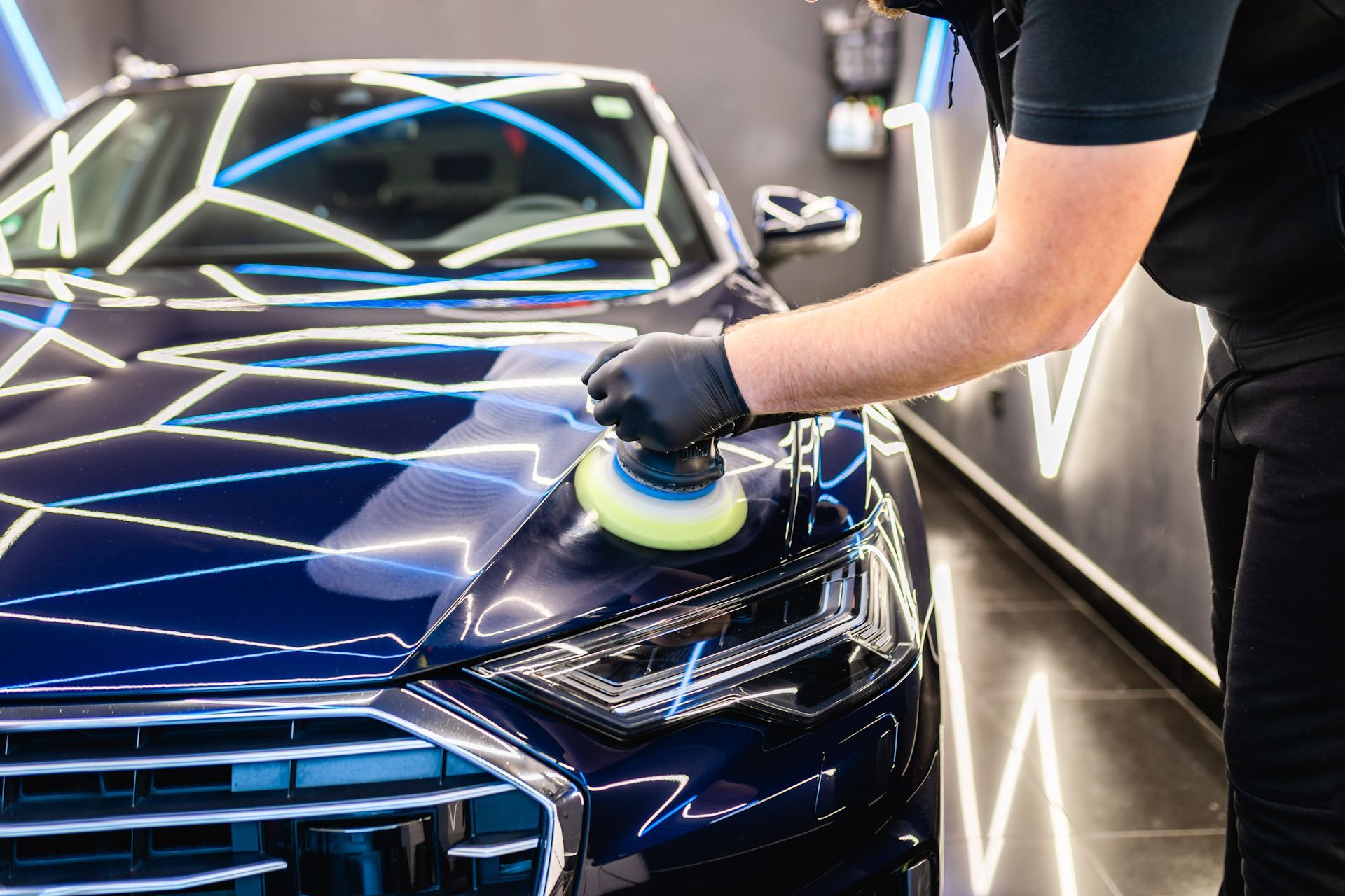 A man is polishing a blue car in a garage.