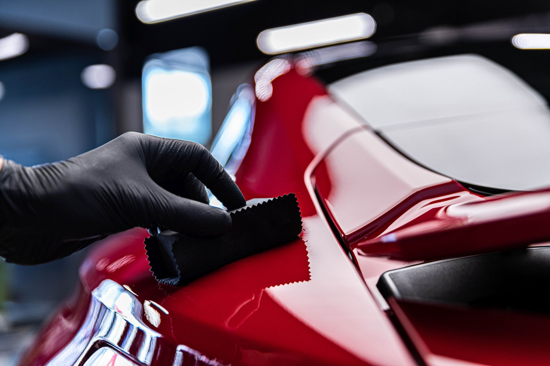 A person wearing black gloves is polishing a red car.