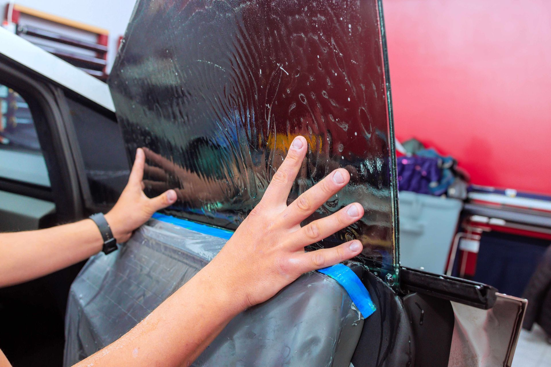 The technician applies window tint film on the car door window.
