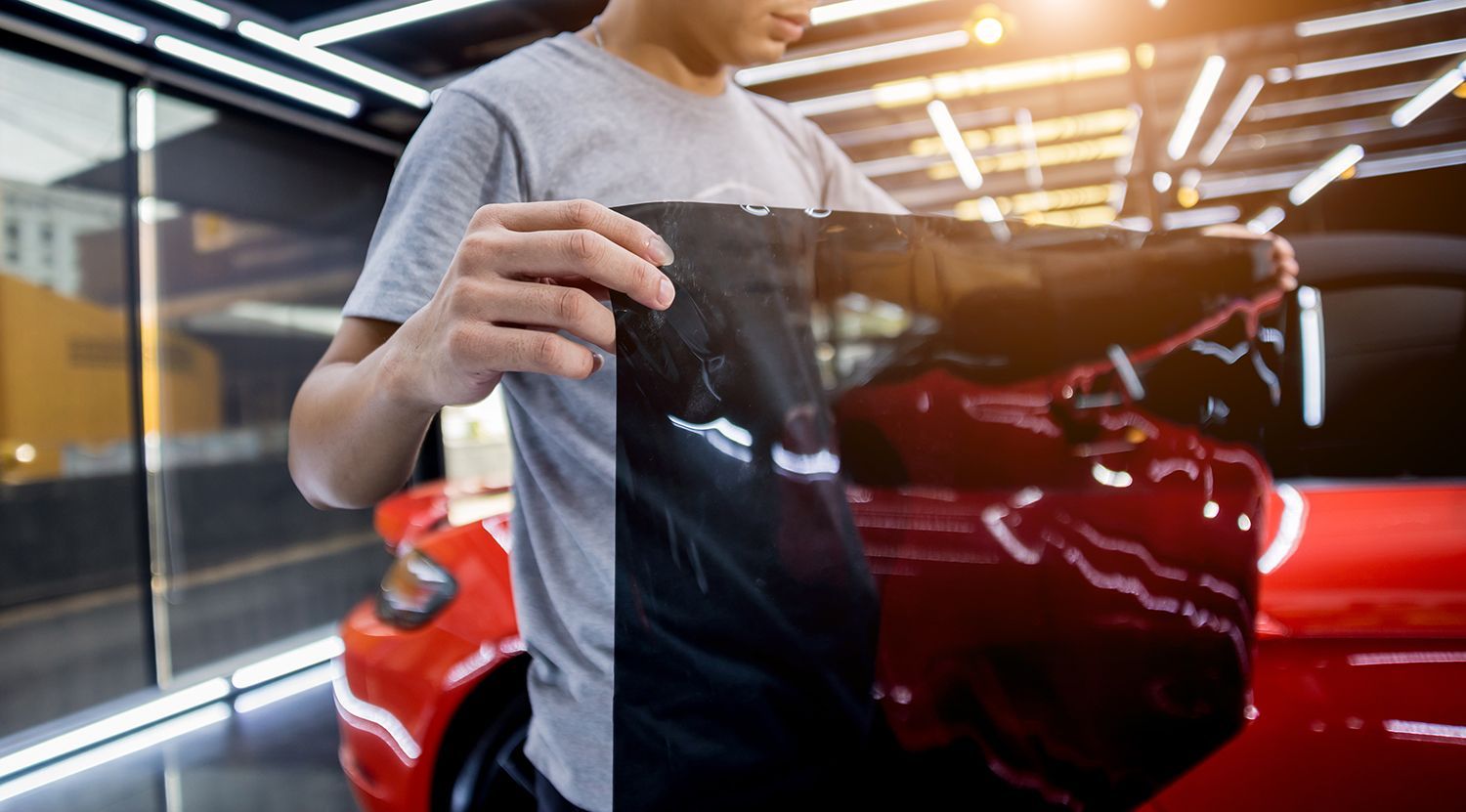 Person holding window tint film in front of a red car in a garage. Person holding window tint film in front of a red car in a garage.