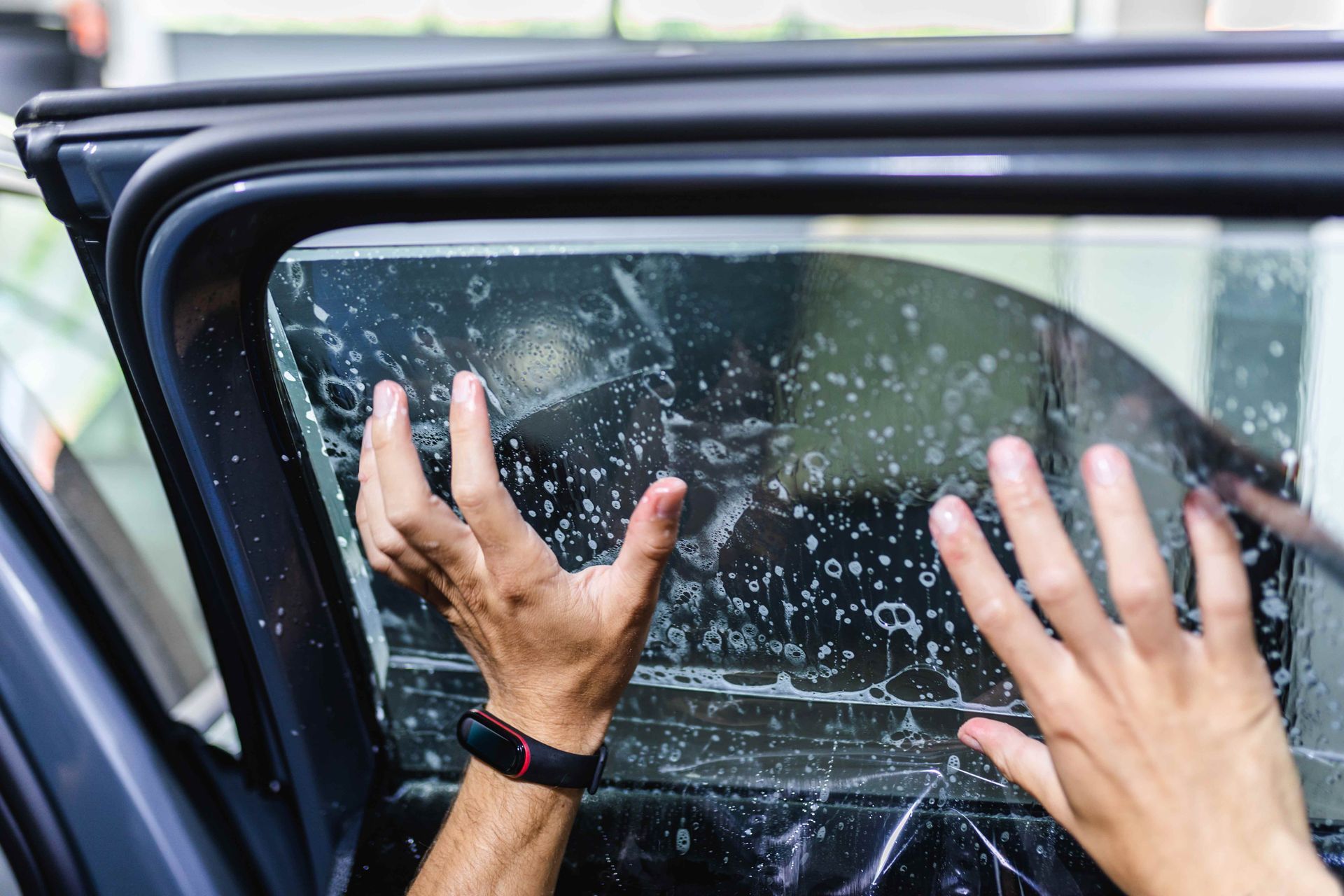 Worker applying tinting foil on car window.