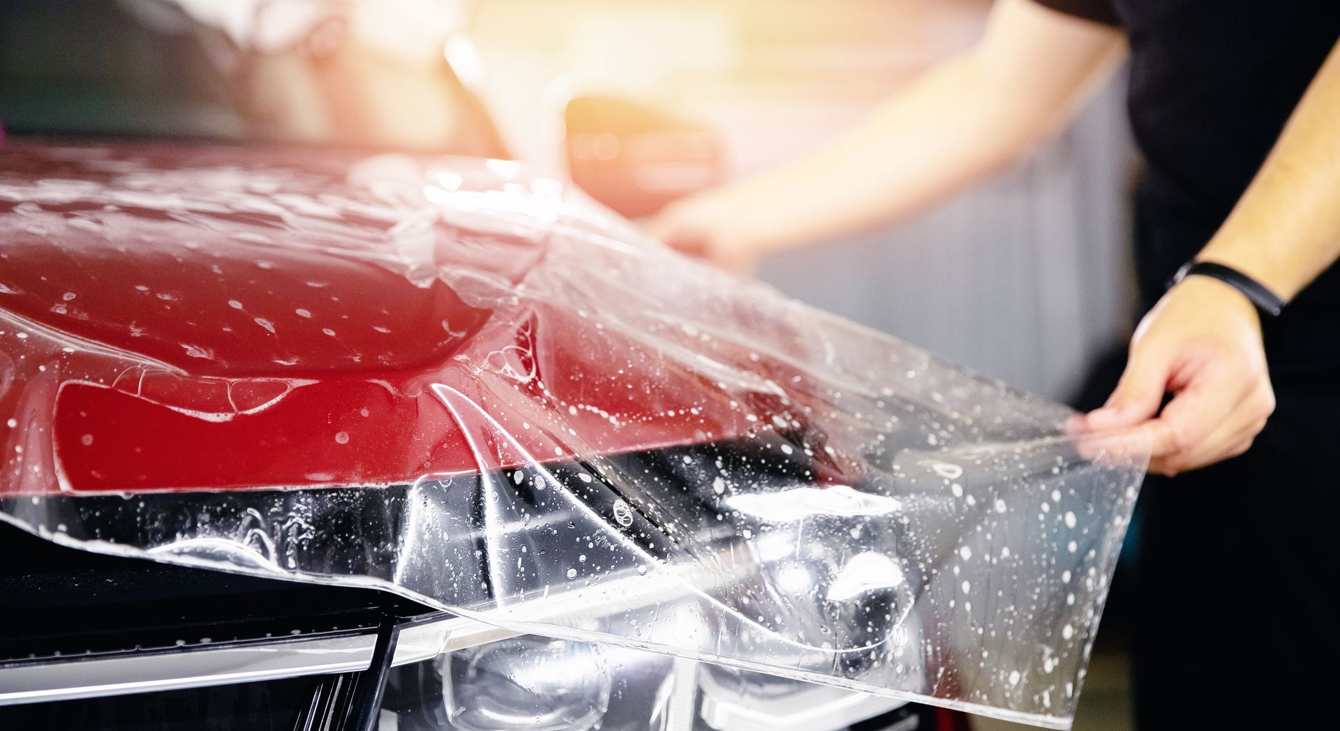 Person applying a clear protective film to the hood of a red car