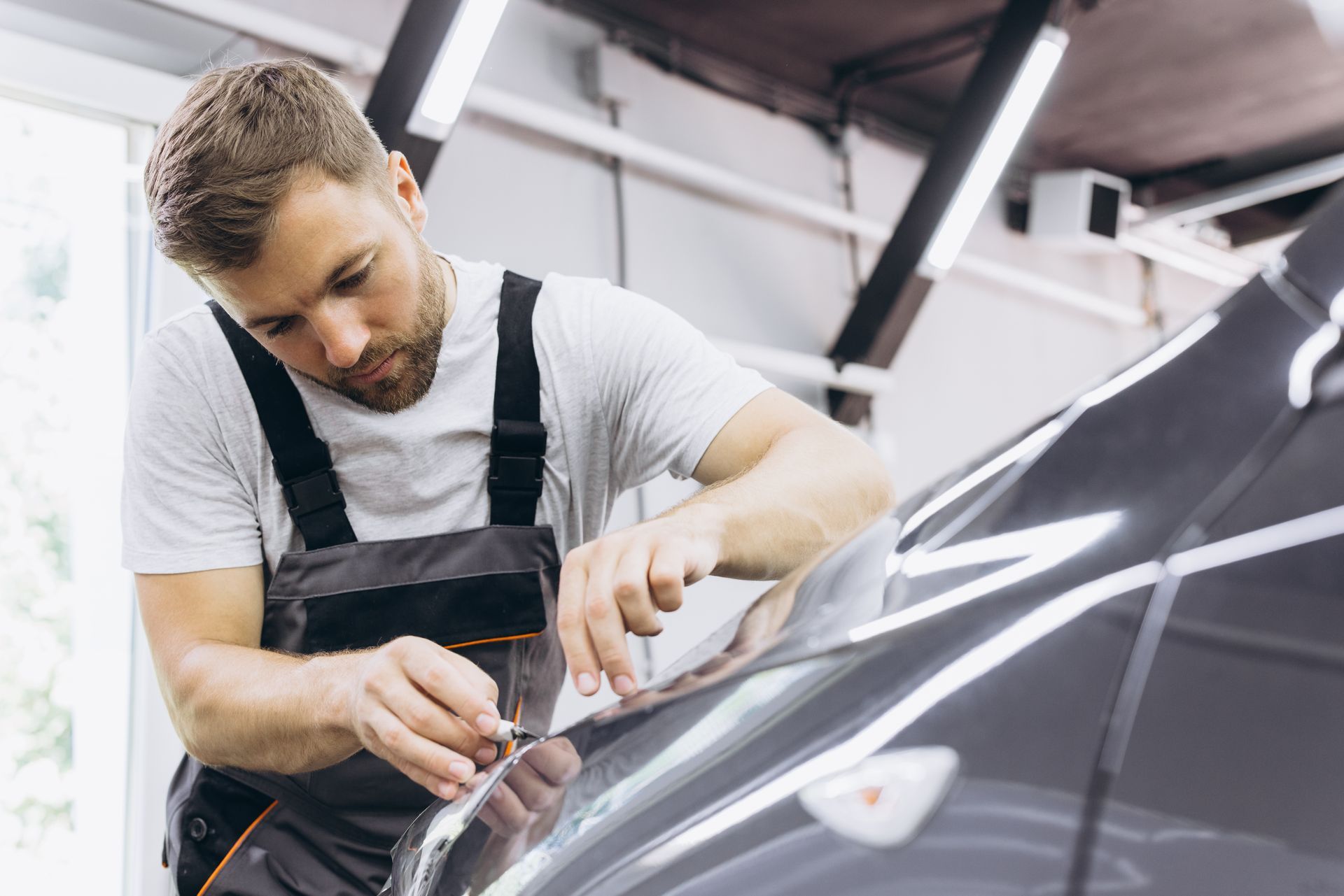 Male specialist cutting and wrapping a car in a garage showroom.