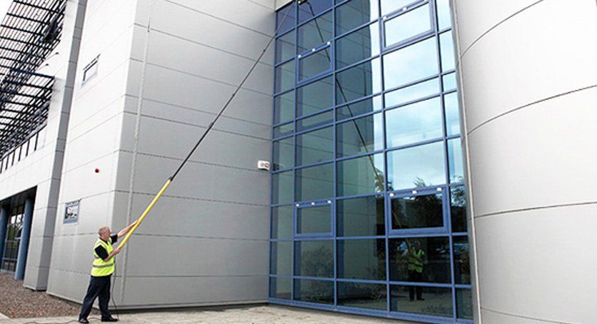 Male staff using long telescopic window cleaner - cleaning commercial window