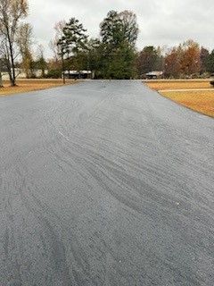 A gray asphalt driveway with trees on the side of it.