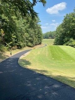 A road leading to a golf course surrounded by trees on a sunny day.