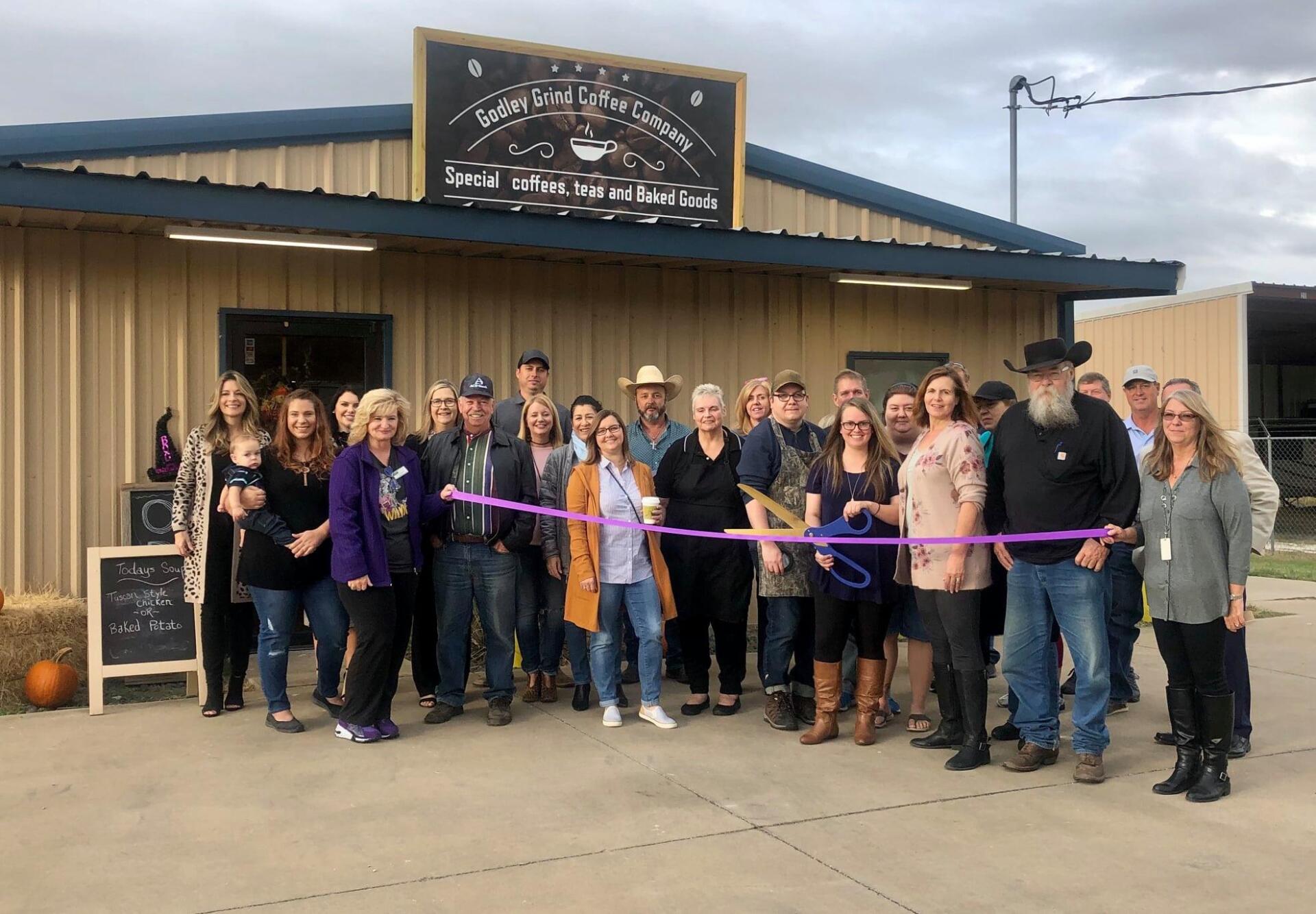 A group of people are standing in front of a building cutting a purple ribbon.