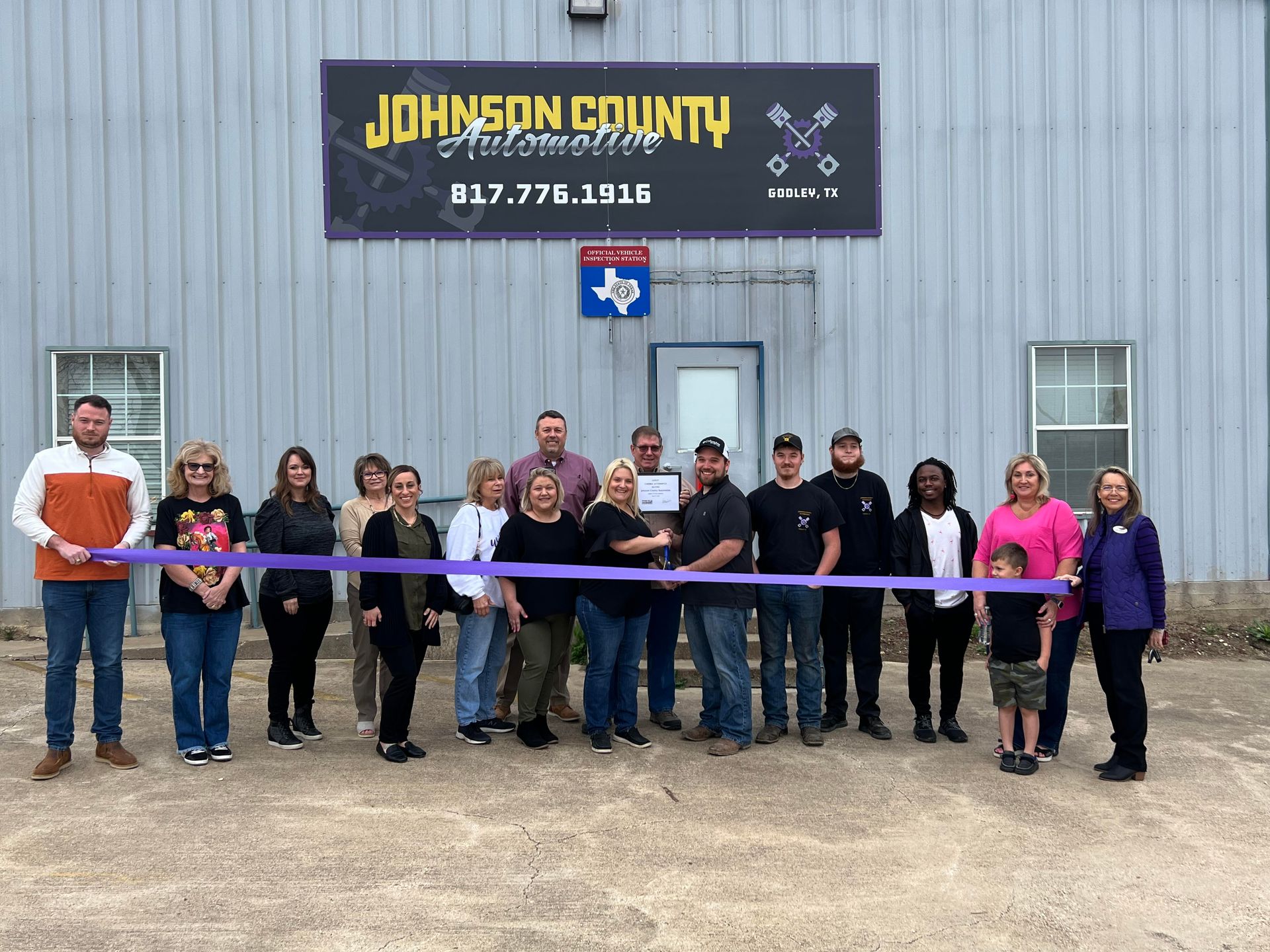 A group of people are standing in front of a building holding a purple ribbon.