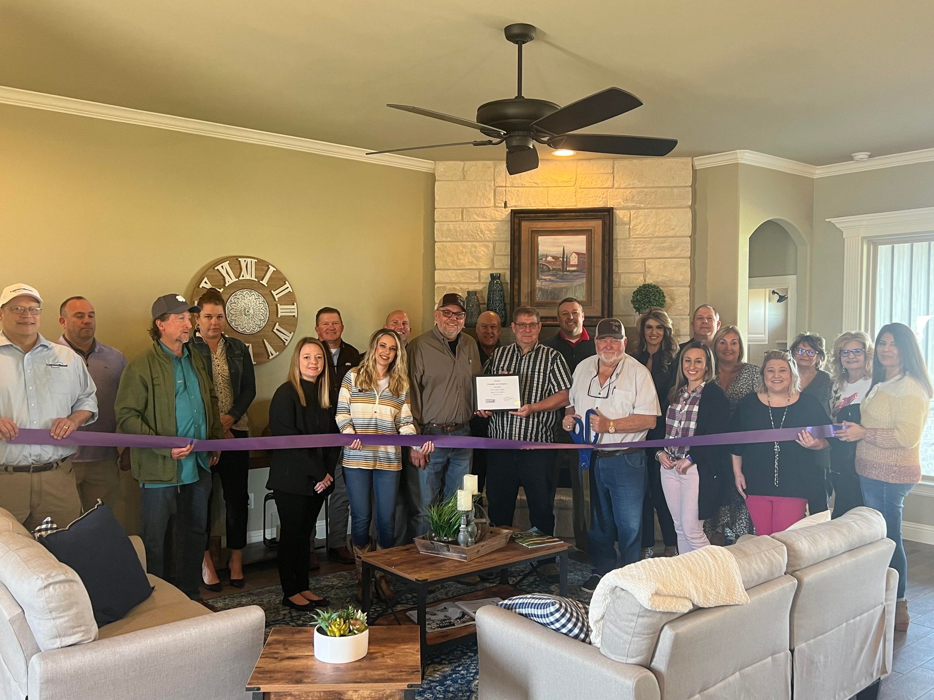 A group of people are cutting a purple ribbon in a living room.