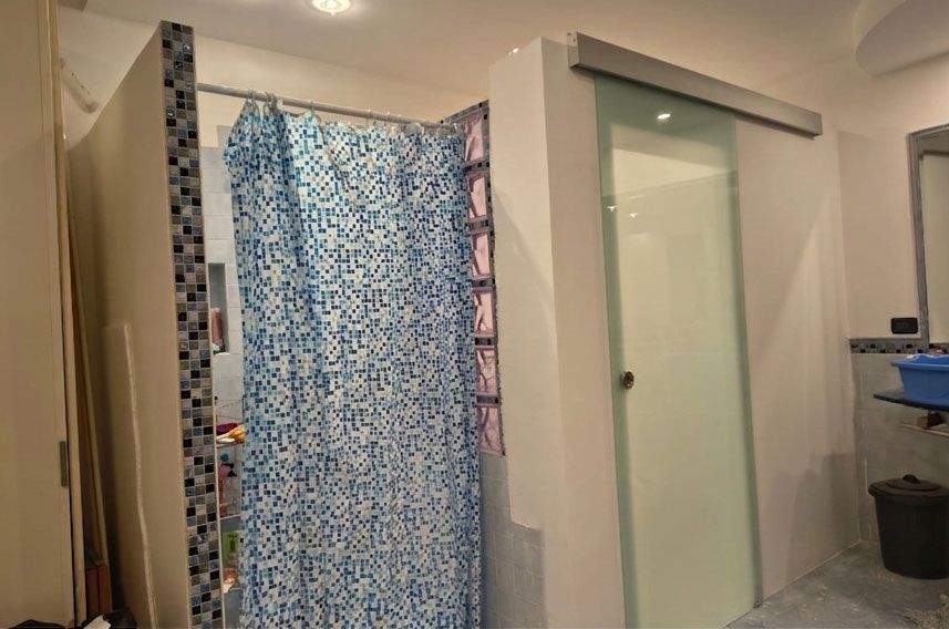 Un bagno dotato di doccia con tenda blu a fantasia e porta scorrevole adiacente in vetro satinato.