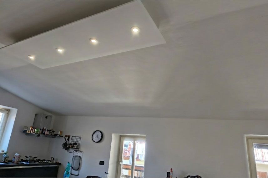 Un pannello rettangolare bianco a soffitto con quattro faretti incassati in una stanza ben illuminata con pareti bianche e un orologio.