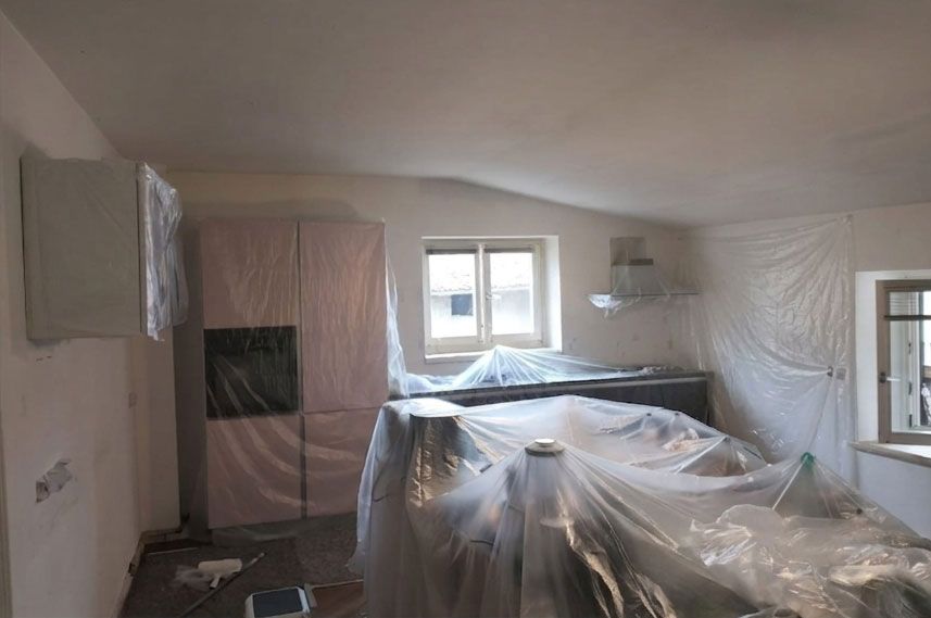 Una stanza interna in fase di ristrutturazione, con pareti, armadi e mobili ricoperti da teli protettivi di plastica.