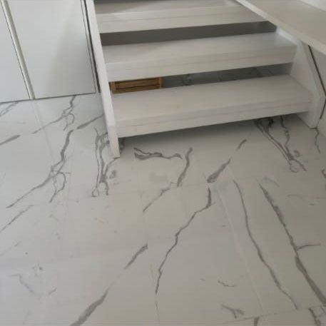 Piastrelle di marmo bianco con venature grigie accanto a una scala in legno bianco.