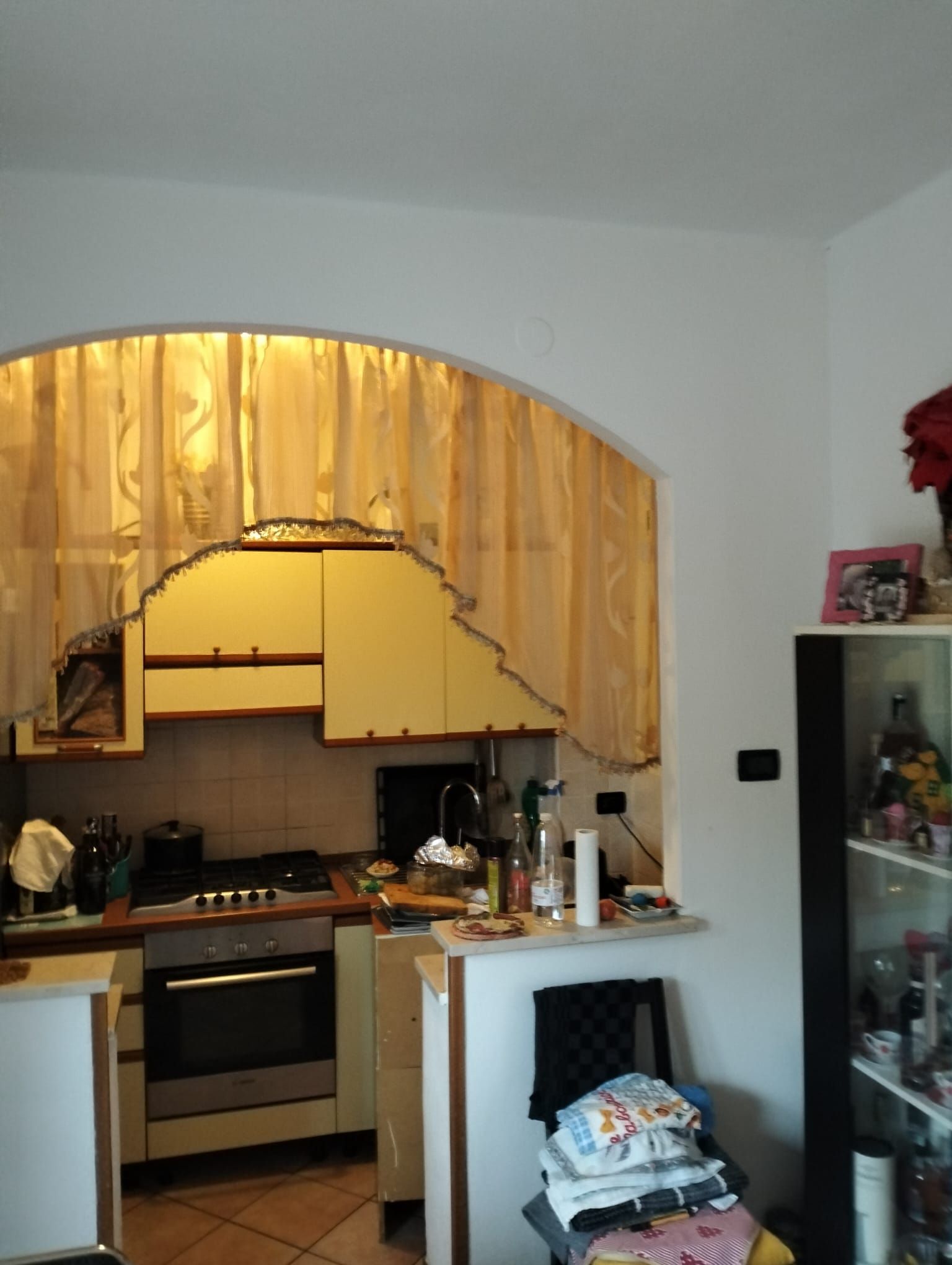 Una cucina con mobili chiari, visibile attraverso un'apertura ad arco, con una tovaglia drappeggiata su una sedia in primo piano.