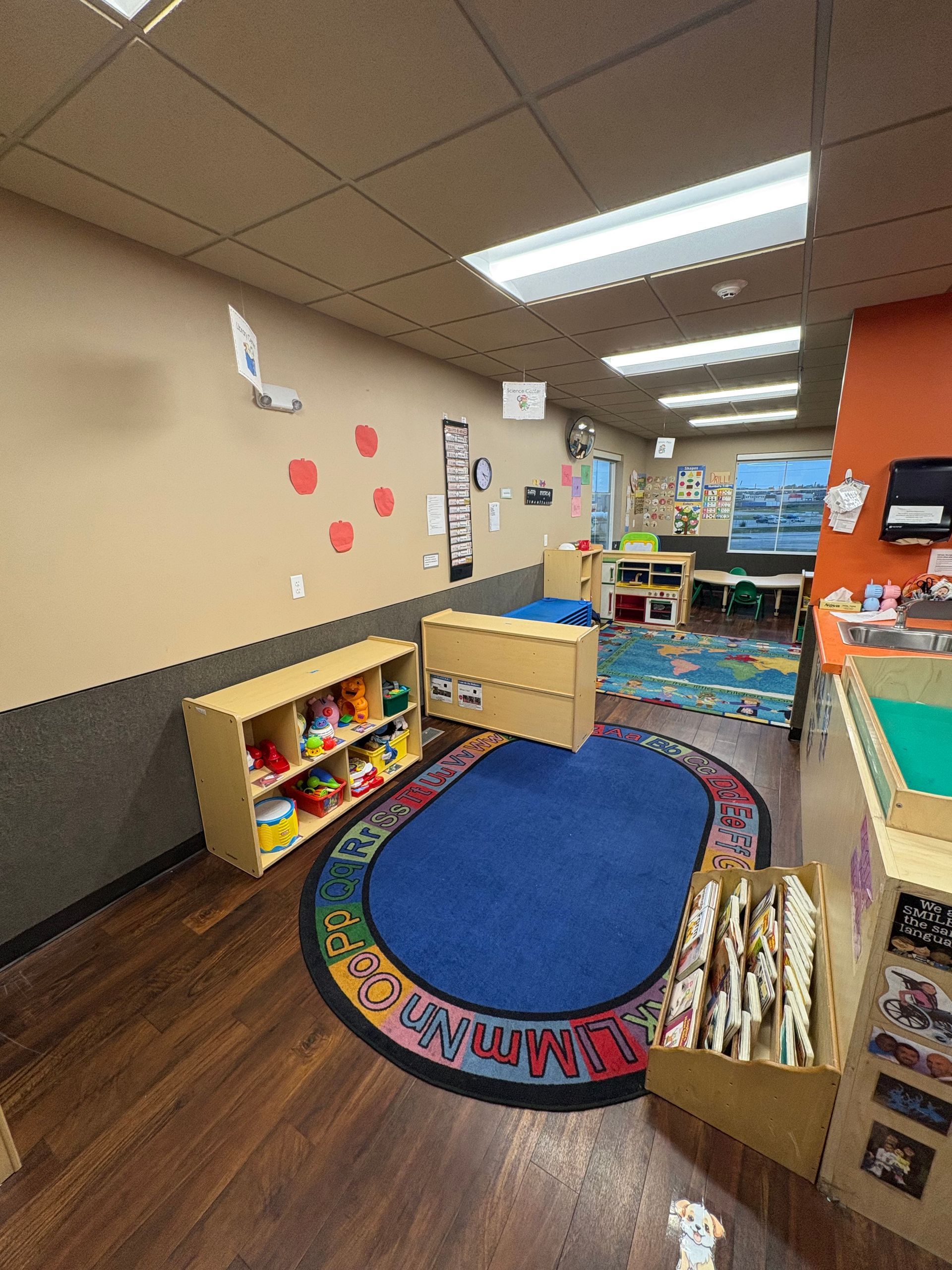 A child's playroom with a blue rug, wooden shelves, and colorful toys.